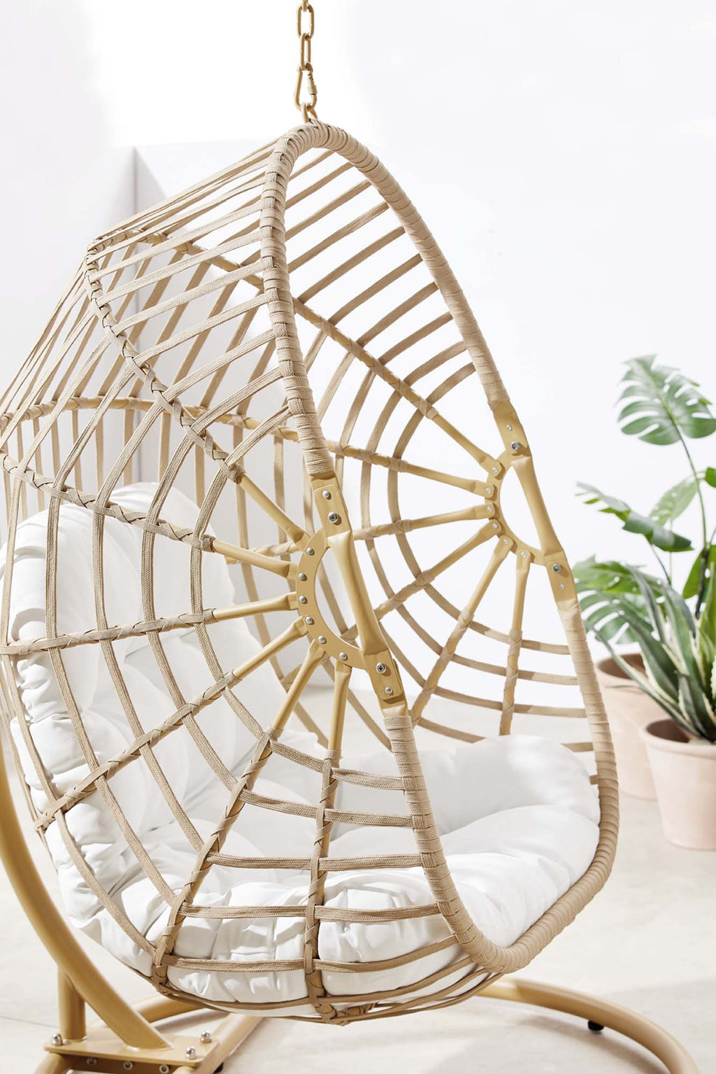 Outdoor hanging wicker swing chair with white cushion, arched seat and lattice sides.