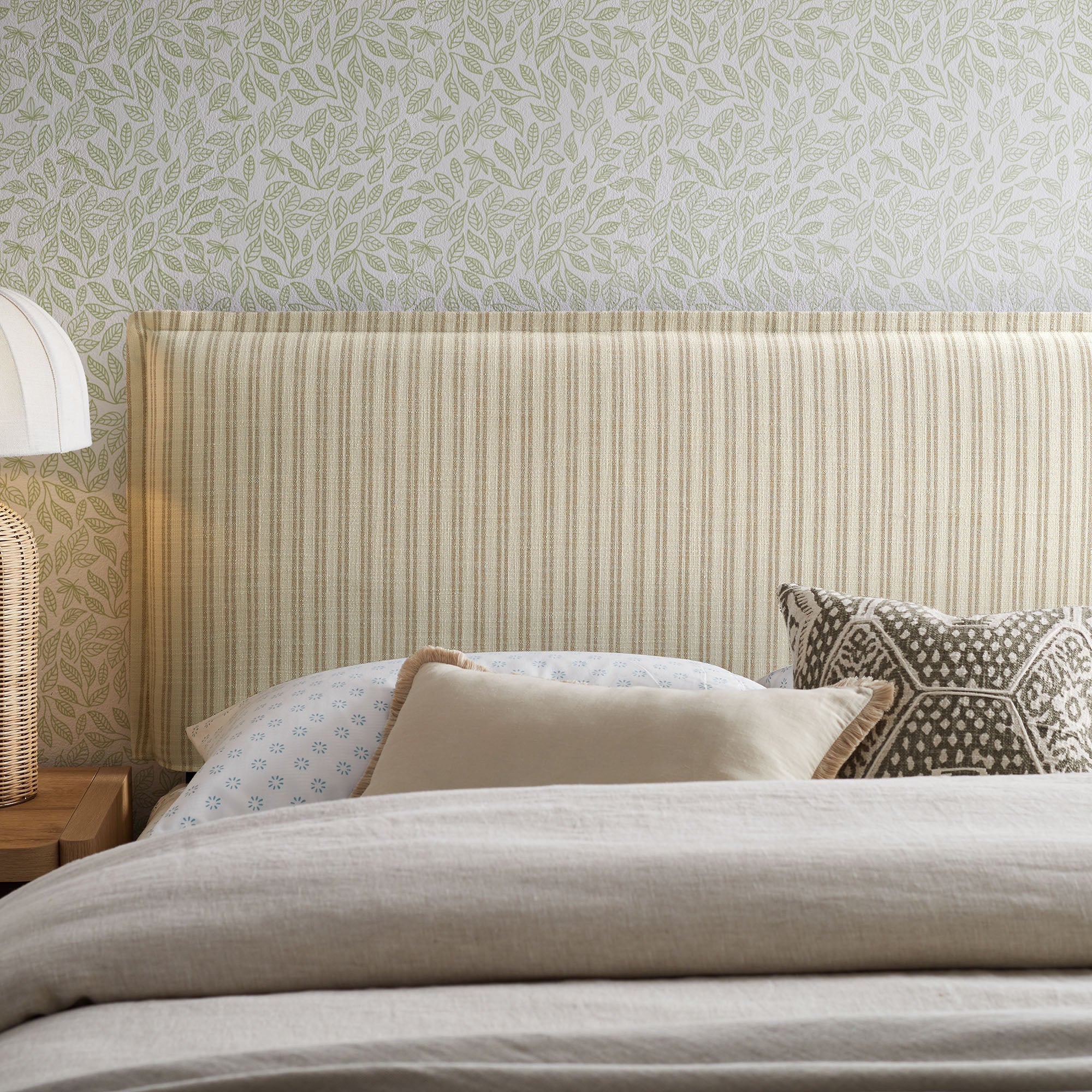 Striped upholstered headboard in cream pinstripe fabric with dark legs behind bed.